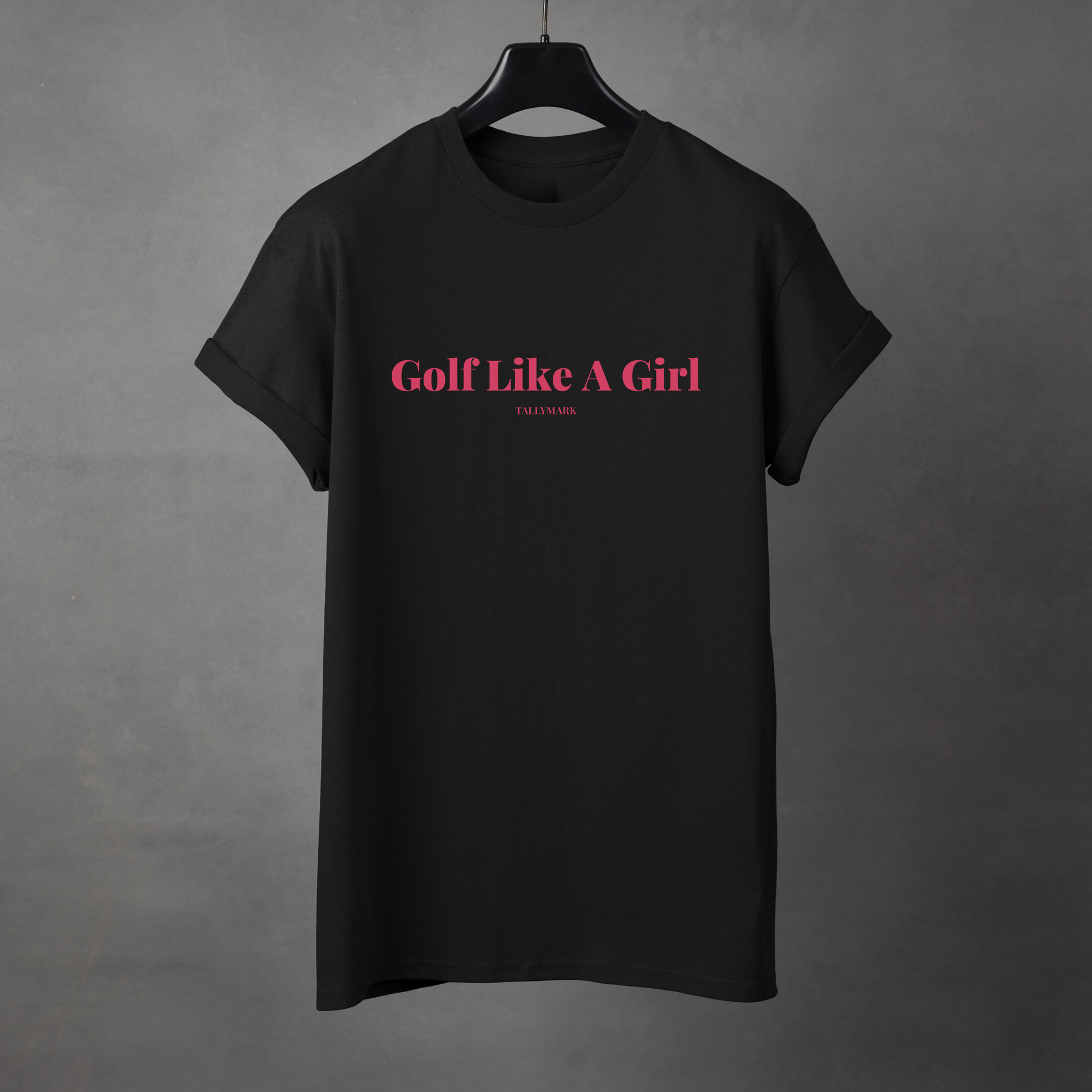 Black t-shirt with pink 'Golf Like A Girl' text against a dark background
