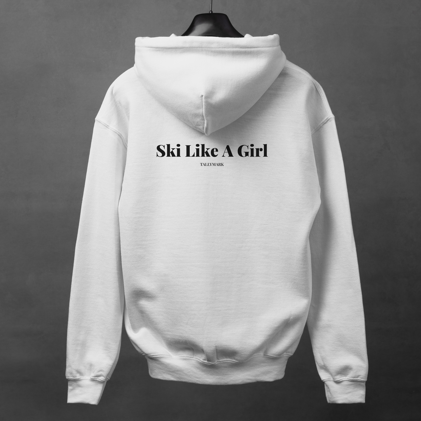 White hoodie with 'Ski Like A Girl' text on the back, displayed on a hanger against a dark background.